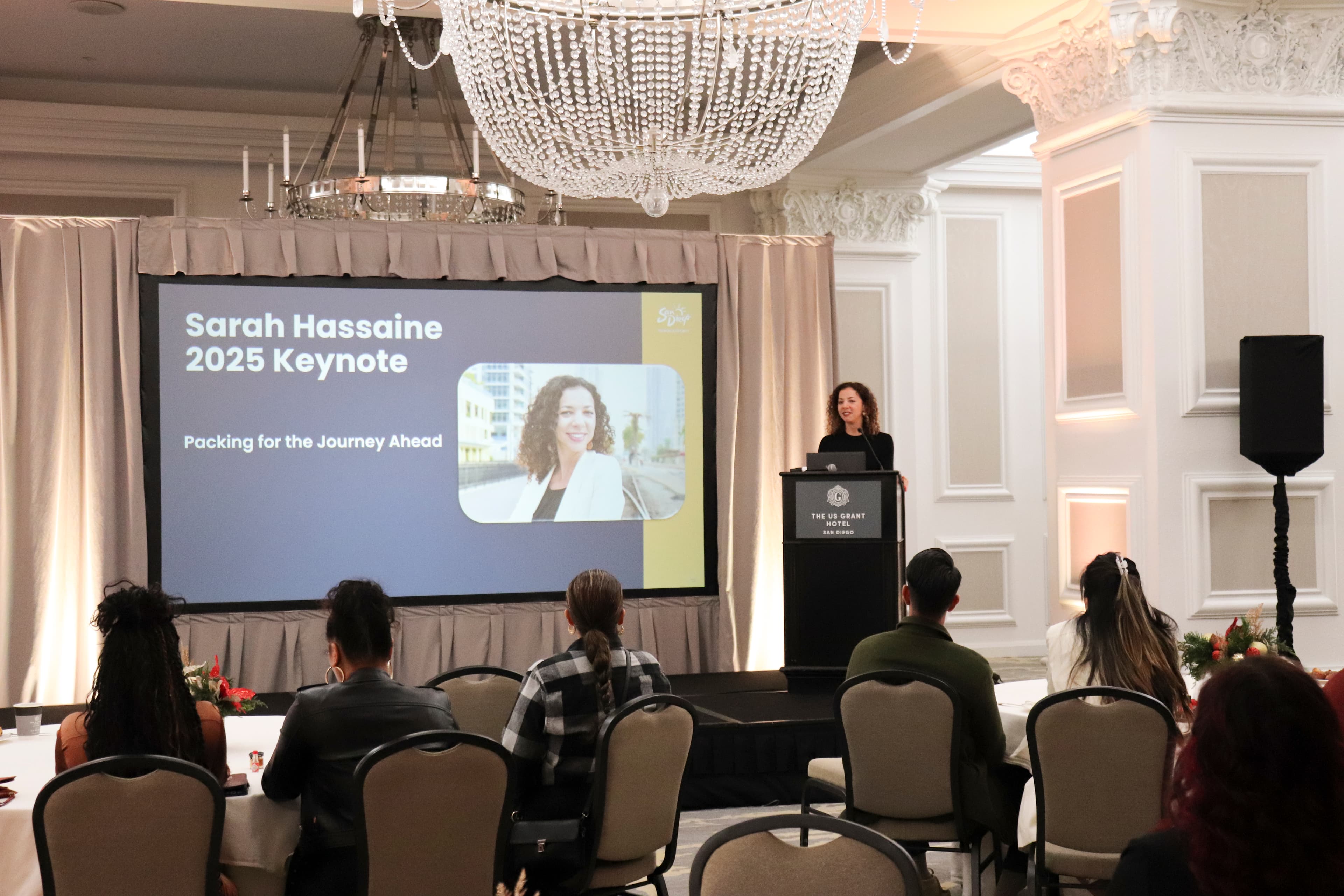 Sarah Hassaine delivers a keynote presentation titled "Packing for the Journey Ahead" in a ballroom.